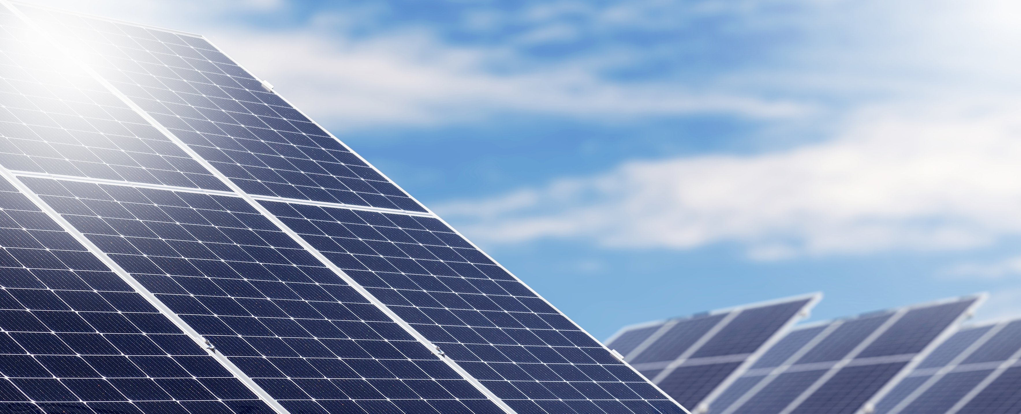 Renewable solar energy farm, big solar panels in a row against blue sky.